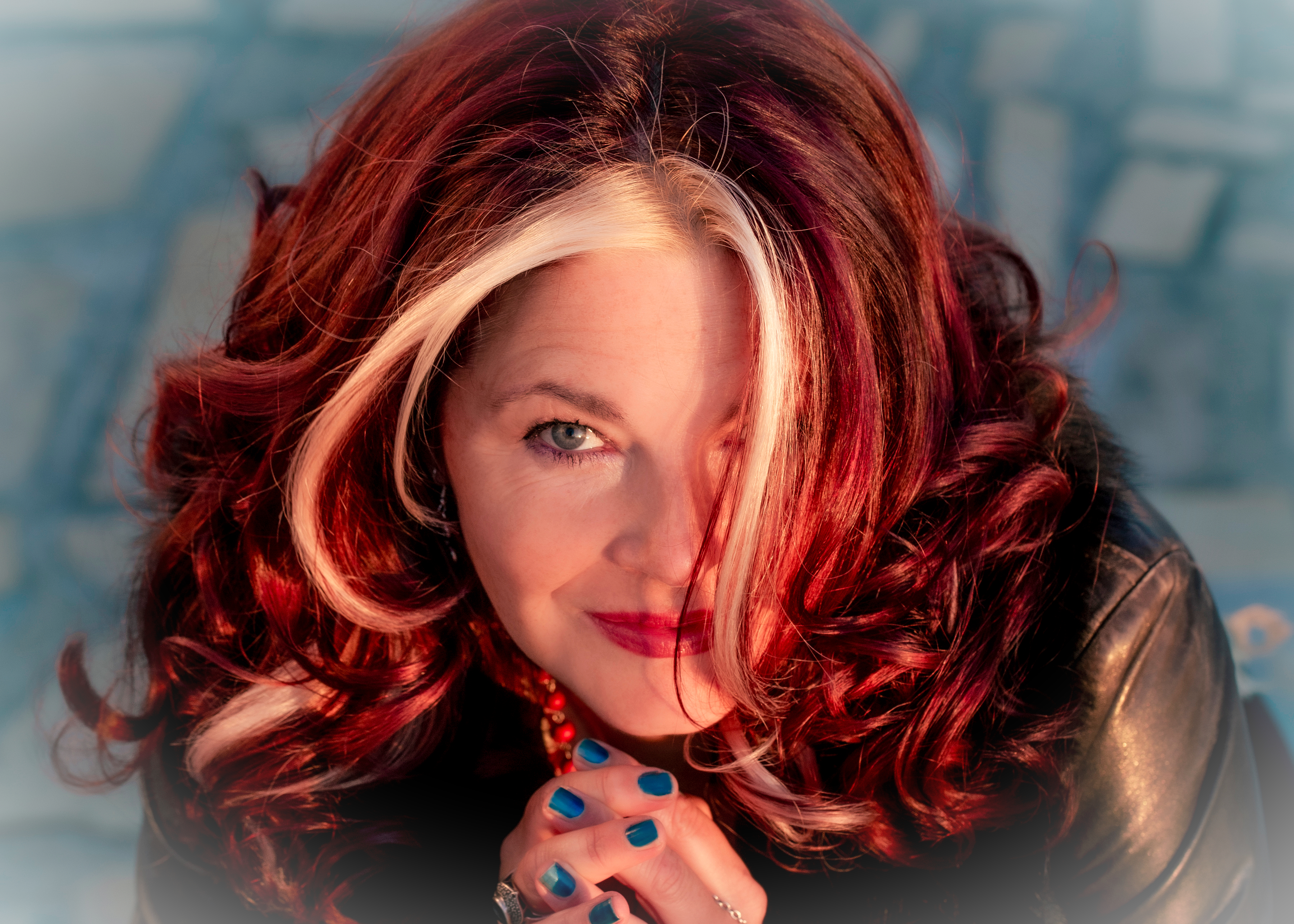 Woman with auburn hair with blonde streaks smiling at the camera and dressed in leather jacket