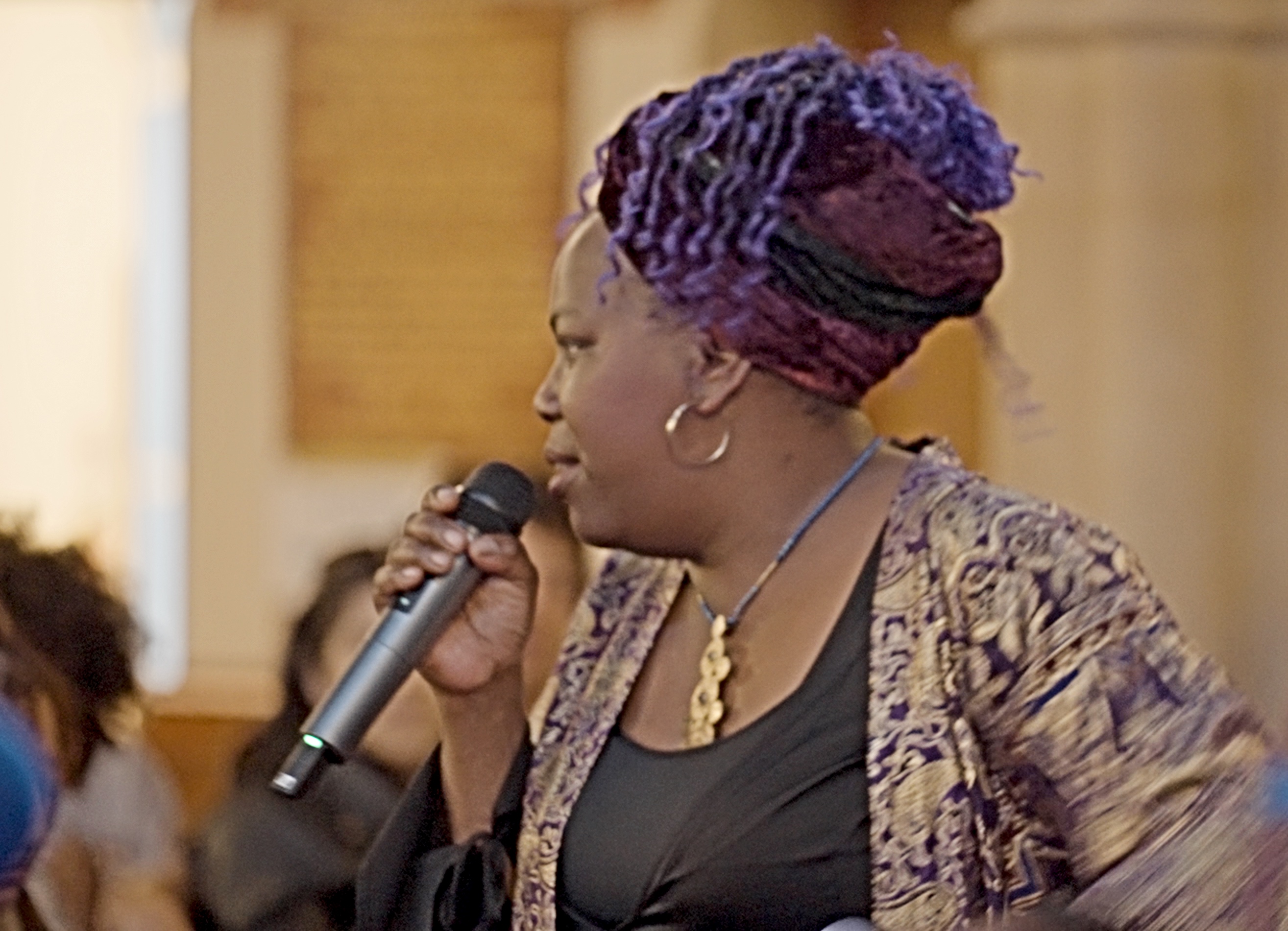 Black woman wearing scarf headdress singing into a microphone