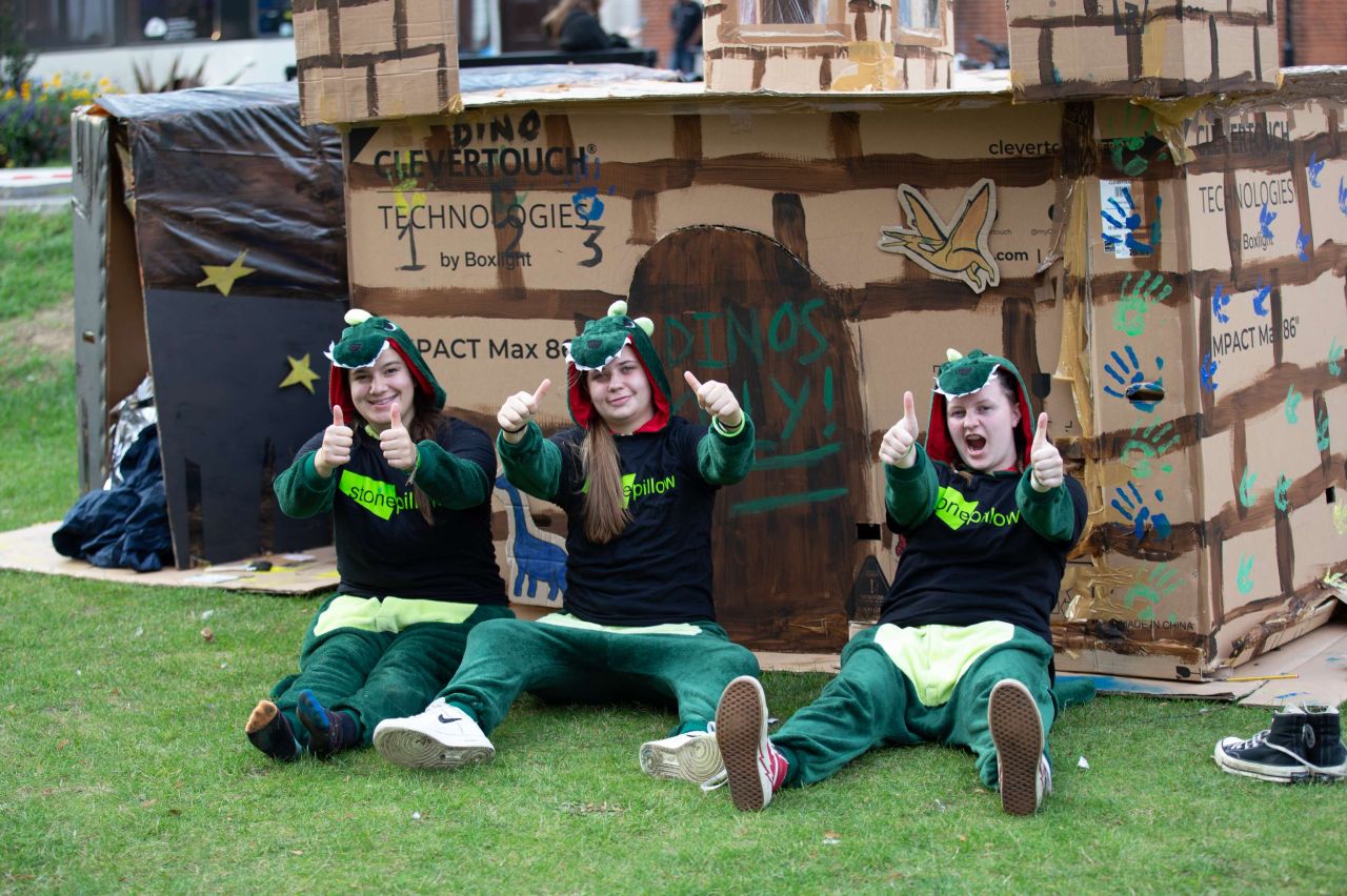 Three women in Stonepillow T-shirts outside their cardboard shelter